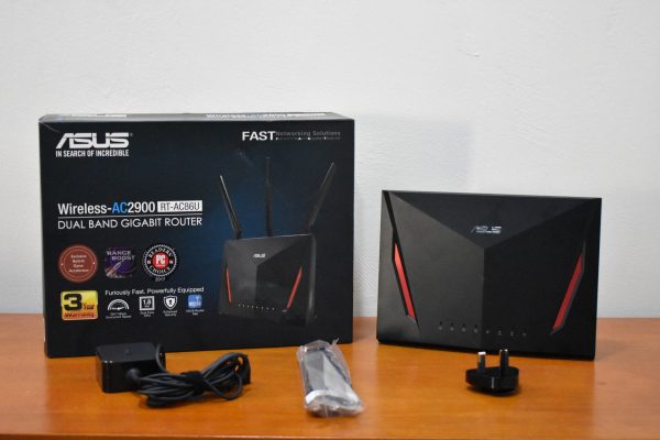 Wi-Fi-роутер Asus RT-AC86U стоит рядом с коробкой и переходниками на столе